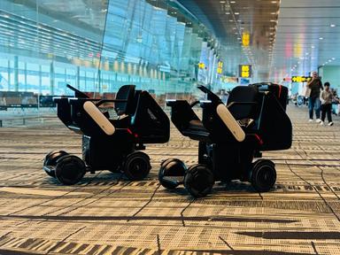 Zwei autonom fahrende WHILL Rollstühle im Transitbereich des Flughafens Changi mit Gates im Hintergrund.