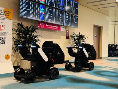 Zwei WHILL Rollstühle des Autonomous Service unter den Fluganzeigetafeln am Flughafen Changi.