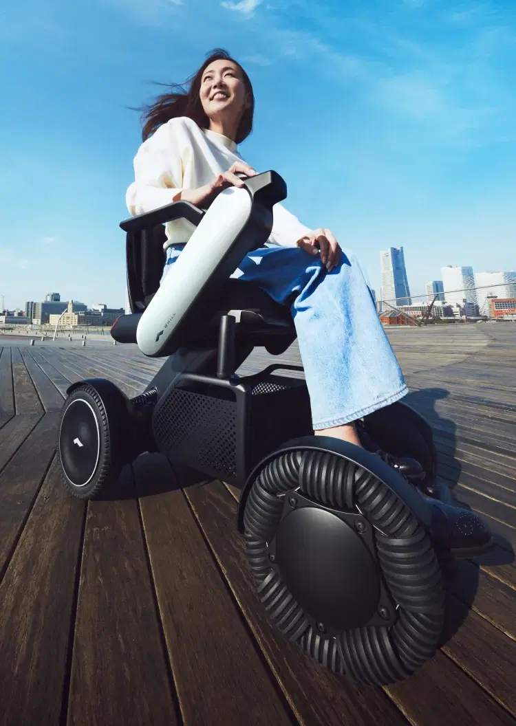 Woman riding a WHILL Model C2 on a waterfront boardwalk
